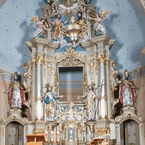 Zdjęcie nr 1: Nastawa ołtarzowa architektoniczna, jednoosiowa, jednokondygnacyjna ze zwieńczeniem, z bramkami i z rocaille&#039;owymi uszami. Tabernakulum w formie zbliżonej do prostopadłościennej skrzynki, na wklęsło-wypukłym rzucie, ustawione na niskim cokole, o wypukłej ściance frontowej. Ujęte jest drewnianą obudową o wklęsłych bokach, flankowane parą ustawionych pod kątem pilastrów, których trzony przyjmują formę wolut. Zwieńczenie tabernakulum w formie niewielkiego szczytu, na którym ustawiona jest pasyjka. Całość ujęta po bokach rocaille&#039;owymi wolutami. Drzwiczki w kształcie stojącego prostokąta, zamknięte łukiem nadwieszonym. W polu, na niebieskim tle malowane przedstawienie kielicha z hostią. Nastawa ustawiona na zdwojonym cokole, o  wklęsłym przebiegu, ujęta dwiema parami kolumn na tle zwielokrotnionych pilastrów. Podpory dźwigają pełne belkowanie, wyłamane pośrodku. Pomiędzy podporami figury: po lewej św. Józefa, a po prawej św. Jana Chrzciciela, nad bramkami: po lewej św. Wojciecha, a po prawej św. Stanisława. Nad tabernakulum rocaille&#039;owy kartusz z łacińską inskrypcją w polu. W polu środkowym nisza w formie stojącego prostokąta, zamkniętego łukiem wklęsło-wypukłym z uskokami z obrazem „Święta Rozmowa”. Zwieńczenie w formie zbliżonej do stojącego prostokąta ujętego po bokach dwoma pilastrami, bogato ozdobione dekoracją rzeźbiarską. W polu przedstawienie Trójcy Świętej, flankowane przez parę aniołów siedzących na wolutowych przyczółkach. Całość zamyka para aniołków ze srebrną wstęgą z napisem „GLORIA IN EXCELSIS DEO”. Bramki z drzwiczkami w formie stojącego prostokąta, flankowane węgarami, zamknięte wolutowym łukiem z zatkniętymi na szczycie rzeźbami świętych. Drzwiczki dekorowane w polu dwiema płycinami. Całość nastawy silnie dekorowana ornamentyką rokokową. Kolumny ustawione na bazach, z kompozytowymi kapitelami, wewnętrzne srebrzone, do jednej trzeciej wysokości zdobione kanelowaniem zamkniętym pierścieniem, kolumny zewnętrzne marmoryzowane. Struktura polichromowana w kolorze beżowym, profilowania marmoryzowane, ornamentyka złocona.