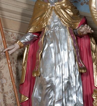 Zdjęcie nr 19: Nastawa ołtarzowa architektoniczna, jednoosiowa, jednokondygnacyjna ze zwieńczeniem, z bramkami i z rocaille&#039;owymi uszami. Tabernakulum w formie zbliżonej do prostopadłościennej skrzynki, na wklęsło-wypukłym rzucie, ustawione na niskim cokole, o wypukłej ściance frontowej. Ujęte jest drewnianą obudową o wklęsłych bokach, flankowane parą ustawionych pod kątem pilastrów, których trzony przyjmują formę wolut. Zwieńczenie tabernakulum w formie niewielkiego szczytu, na którym ustawiona jest pasyjka. Całość ujęta po bokach rocaille&#039;owymi wolutami. Drzwiczki w kształcie stojącego prostokąta, zamknięte łukiem nadwieszonym. W polu, na niebieskim tle malowane przedstawienie kielicha z hostią. Nastawa ustawiona na zdwojonym cokole, o  wklęsłym przebiegu, ujęta dwiema parami kolumn na tle zwielokrotnionych pilastrów. Podpory dźwigają pełne belkowanie, wyłamane pośrodku. Pomiędzy podporami figury: po lewej św. Józefa, a po prawej św. Jana Chrzciciela, nad bramkami: po lewej św. Wojciecha, a po prawej św. Stanisława. Nad tabernakulum rocaille&#039;owy kartusz z łacińską inskrypcją w polu. W polu środkowym nisza w formie stojącego prostokąta, zamkniętego łukiem wklęsło-wypukłym z uskokami z obrazem „Święta Rozmowa”. Zwieńczenie w formie zbliżonej do stojącego prostokąta ujętego po bokach dwoma pilastrami, bogato ozdobione dekoracją rzeźbiarską. W polu przedstawienie Trójcy Świętej, flankowane przez parę aniołów siedzących na wolutowych przyczółkach. Całość zamyka para aniołków ze srebrną wstęgą z napisem „GLORIA IN EXCELSIS DEO”. Bramki z drzwiczkami w formie stojącego prostokąta, flankowane węgarami, zamknięte wolutowym łukiem z zatkniętymi na szczycie rzeźbami świętych. Drzwiczki dekorowane w polu dwiema płycinami. Całość nastawy silnie dekorowana ornamentyką rokokową. Kolumny ustawione na bazach, z kompozytowymi kapitelami, wewnętrzne srebrzone, do jednej trzeciej wysokości zdobione kanelowaniem zamkniętym pierścieniem, kolumny zewnętrzne marmoryzowane. Struktura polichromowana w kolorze beżowym, profilowania marmoryzowane, ornamentyka złocona.