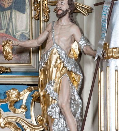 Zdjęcie nr 17: Nastawa ołtarzowa architektoniczna, jednoosiowa, jednokondygnacyjna ze zwieńczeniem, z bramkami i z rocaille'owymi uszami. Tabernakulum w formie zbliżonej do prostopadłościennej skrzynki, na wklęsło-wypukłym rzucie, ustawione na niskim cokole, o wypukłej ściance frontowej. Ujęte jest drewnianą obudową o wklęsłych bokach, flankowane parą ustawionych pod kątem pilastrów, których trzony przyjmują formę wolut. Zwieńczenie tabernakulum w formie niewielkiego szczytu, na którym ustawiona jest pasyjka. Całość ujęta po bokach rocaille'owymi wolutami. Drzwiczki w kształcie stojącego prostokąta, zamknięte łukiem nadwieszonym. W polu, na niebieskim tle malowane przedstawienie kielicha z hostią. Nastawa ustawiona na zdwojonym cokole, o  wklęsłym przebiegu, ujęta dwiema parami kolumn na tle zwielokrotnionych pilastrów. Podpory dźwigają pełne belkowanie, wyłamane pośrodku. Pomiędzy podporami figury: po lewej św. Józefa, a po prawej św. Jana Chrzciciela, nad bramkami: po lewej św. Wojciecha, a po prawej św. Stanisława. Nad tabernakulum rocaille'owy kartusz z łacińską inskrypcją w polu. W polu środkowym nisza w formie stojącego prostokąta, zamkniętego łukiem wklęsło-wypukłym z uskokami z obrazem „Święta Rozmowa”. Zwieńczenie w formie zbliżonej do stojącego prostokąta ujętego po bokach dwoma pilastrami, bogato ozdobione dekoracją rzeźbiarską. W polu przedstawienie Trójcy Świętej, flankowane przez parę aniołów siedzących na wolutowych przyczółkach. Całość zamyka para aniołków ze srebrną wstęgą z napisem „GLORIA IN EXCELSIS DEO”. Bramki z drzwiczkami w formie stojącego prostokąta, flankowane węgarami, zamknięte wolutowym łukiem z zatkniętymi na szczycie rzeźbami świętych. Drzwiczki dekorowane w polu dwiema płycinami. Całość nastawy silnie dekorowana ornamentyką rokokową. Kolumny ustawione na bazach, z kompozytowymi kapitelami, wewnętrzne srebrzone, do jednej trzeciej wysokości zdobione kanelowaniem zamkniętym pierścieniem, kolumny zewnętrzne marmoryzowane. Struktura polichromowana w kolorze beżowym, profilowania marmoryzowane, ornamentyka złocona.