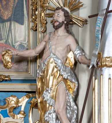 Zdjęcie nr 1: Rzeźba ustawiona na niskim postumencie. Święty ukazany w postawie stojącej w kontrapoście, z lewą nogą ugiętą w kolanie, z krzyżem w lewej dłoni oraz niezidentyfikowanym przedmiotem w prawej dłoni (muszla?), z głową zwróconą delikatnie w prawo. Twarz szczupła, okolona krótką, ciemnobrązową brodą, długi i wąski nos, wzrok skierowany w prawo i ku górze. Włosy długie, ciemnobrązowe, kręcone, spływające na plecy. Wokół głowy promienisty nimb. Święty jest ubrany w skórę wielbłądzią zawieszoną na pasku na prawym ramieniu, odsłaniającą nagi tors i lewą nogę. Krzyż prosty z pionową banderolą z napisem „ECCE AGNUS DEI”. Polichromia w odsłoniętych partiach ciała naturalistyczna, szaty i detale złocone i srebrzone.

