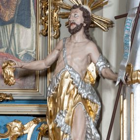 Zdjęcie nr 1: Rzeźba ustawiona na niskim postumencie. Święty ukazany w postawie stojącej w kontrapoście, z lewą nogą ugiętą w kolanie, z krzyżem w lewej dłoni oraz niezidentyfikowanym przedmiotem w prawej dłoni (muszla?), z głową zwróconą delikatnie w prawo. Twarz szczupła, okolona krótką, ciemnobrązową brodą, długi i wąski nos, wzrok skierowany w prawo i ku górze. Włosy długie, ciemnobrązowe, kręcone, spływające na plecy. Wokół głowy promienisty nimb. Święty jest ubrany w skórę wielbłądzią zawieszoną na pasku na prawym ramieniu, odsłaniającą nagi tors i lewą nogę. Krzyż prosty z pionową banderolą z napisem „ECCE AGNUS DEI”. Polichromia w odsłoniętych partiach ciała naturalistyczna, szaty i detale złocone i srebrzone.
