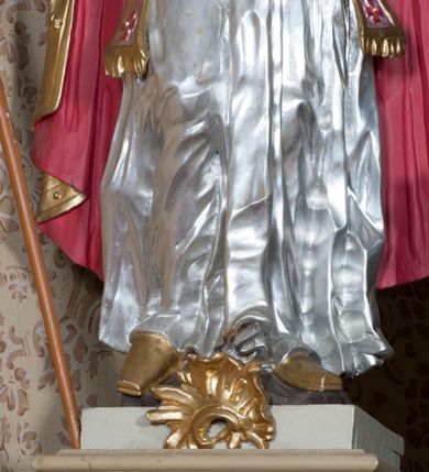 Zdjęcie nr 3: Rzeźba ustawiona na niskim, prostopadłościennym cokole przedstawiająca św. Stanisława w postawie stojącej, w delikatnym kontrapoście, z prawa nogą ugiętą w kolanie, z krzyżem w prawej dłoni, z lewą ręką odsuniętą delikatnie w bok, z głową skierowaną ku górze. Twarz podłużna, okolona średniej długości, ciemnobrązową, bujną brodą, oczy skierowane ku górze, nos długi i szeroki, włosy średniej długości, kręcone. Święty jest ubrany w albę z długimi rękawami oraz złoconą kapę z czerwoną podszewką spiętą na piersi klamrą, spod kapy widoczna czerwona stuła, na stopach złocone buty, a na głowie infuła. Polichromia w odsłoniętych partiach ciała naturalistyczna. 