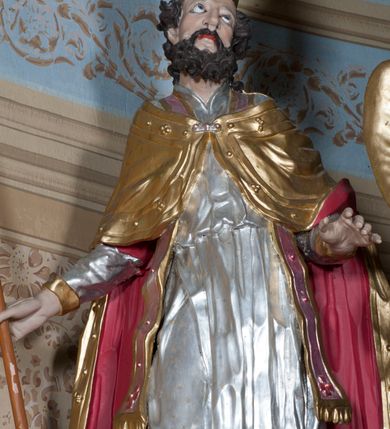 Zdjęcie nr 1: Rzeźba ustawiona na niskim, prostopadłościennym cokole przedstawiająca św. Stanisława w postawie stojącej, w delikatnym kontrapoście, z prawa nogą ugiętą w kolanie, z krzyżem w prawej dłoni, z lewą ręką odsuniętą delikatnie w bok, z głową skierowaną ku górze. Twarz podłużna, okolona średniej długości, ciemnobrązową, bujną brodą, oczy skierowane ku górze, nos długi i szeroki, włosy średniej długości, kręcone. Święty jest ubrany w albę z długimi rękawami oraz złoconą kapę z czerwoną podszewką spiętą na piersi klamrą, spod kapy widoczna czerwona stuła, na stopach złocone buty, a na głowie infuła. Polichromia w odsłoniętych partiach ciała naturalistyczna. 