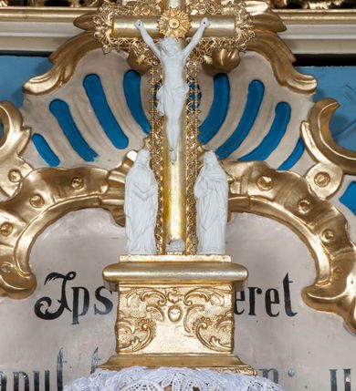 Zdjęcie nr 2: Tabernakulum w formie zbliżonej do prostopadłościennej skrzynki, na wklęsło-wypukłym rzucie, ustawione na niskim cokole, o wypukłej ściance frontowej, ujęte drewnianą obudową o wklęsłych bokach, flankowane parą ustawionych pod kątem pilastrów, których trzony przyjmują formę wolut. Zwieńczenie tabernakulum w formie niewielkiego szczytu, na którym ustawiona jest pasyjka. Całość ujęta po bokach rocaille&#039;owymi wolutami. Drzwiczki w kształcie stojącego prostokąta, zamknięte łukiem nadwieszonym. W polu, na niebieskim tle malowane przedstawienie kielicha z hostią. Struktura polichromowana na kolor jasnobeżowy, detale na kolor ciemnobeżowy, cokół marmoryzowany, ornamentyka złocona.