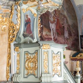 Zdjęcie nr 1: Ambona przyścienna, wisząca, z dostępem od strony prezbiterium w postaci jednobiegowych schodów z pełną balustradą dekorowaną dwoma płycinami w kształcie rombów oraz poręczą w formie gzymsu, zakończoną filarem z rokokowym wazonem. Kosz na planie kwadratu o ściętych narożach i wklęsłych bokach, na profilowanym cokole; u spodu podwieszony ostrosłup o wklęsłych bokach, z wolutami w narożach, zakończony szyszką w formie rocaille'u. Ścianki kosza flankowane pilastrami w formie spływów wolutowych z płyciną pośrodku w kształcie stojącego prostokąta o wklęsłych górnych i spodnich bokach; w polu ścianek kosza płyciny analogiczne jak na spływach wolutowych z dekoracją rocaille'ową w polu. Parapet w postaci profilowanego gzymsu. Zaplecek w kształcie stojącego prostokąta o wklęsłych bokach, ujętych spływami wolutowymi. W polu obraz Chrystusa Dobrego Pasterza umieszczony w płycinie w formie stojącego prostokąta o wklęsłych bokach, zamkniętego łukiem nadwieszonym z uskokami; u góry rocaille i rozety. Zaplecek flankowany uszami w postaci strzępionych liści. Baldachim na planie analogicznym jak kosz w postaci pełnego belkowania dekorowanego ornamentem rocaille'owym. Belkowanie stanowi podstawę dla czterech wolutowych kabłąków, dźwigających cokół z rokokowym wazonem. U spodu baldachimu rzeźbiona gołębica Ducha Świętego w promienistej glorii. Struktura polichromowana w kolorze seledynowym z ciemniejszymi profilami, ornamentyka złocona, gołębica srebrzona.