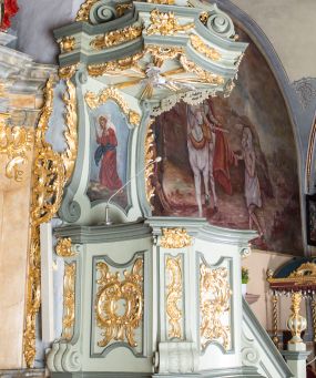 Zdjęcie nr 1: Ambona przyścienna, wisząca, z dostępem od strony prezbiterium w postaci jednobiegowych schodów z pełną balustradą dekorowaną dwoma płycinami w kształcie rombów oraz poręczą w formie gzymsu, zakończoną filarem z rokokowym wazonem. Kosz na planie kwadratu o ściętych narożach i wklęsłych bokach, na profilowanym cokole; u spodu podwieszony ostrosłup o wklęsłych bokach, z wolutami w narożach, zakończony szyszką w formie rocaille'u. Ścianki kosza flankowane pilastrami w formie spływów wolutowych z płyciną pośrodku w kształcie stojącego prostokąta o wklęsłych górnych i spodnich bokach; w polu ścianek kosza płyciny analogiczne jak na spływach wolutowych z dekoracją rocaille'ową w polu. Parapet w postaci profilowanego gzymsu. Zaplecek w kształcie stojącego prostokąta o wklęsłych bokach, ujętych spływami wolutowymi. W polu obraz Chrystusa Dobrego Pasterza umieszczony w płycinie w formie stojącego prostokąta o wklęsłych bokach, zamkniętego łukiem nadwieszonym z uskokami; u góry rocaille i rozety. Zaplecek flankowany uszami w postaci strzępionych liści. Baldachim na planie analogicznym jak kosz w postaci pełnego belkowania dekorowanego ornamentem rocaille'owym. Belkowanie stanowi podstawę dla czterech wolutowych kabłąków, dźwigających cokół z rokokowym wazonem. U spodu baldachimu rzeźbiona gołębica Ducha Świętego w promienistej glorii. Struktura polichromowana w kolorze seledynowym z ciemniejszymi profilami, ornamentyka złocona, gołębica srebrzona.
