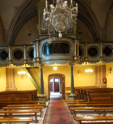 Zdjęcie nr 1: Chór muzyczny architektoniczny, siedmioosiowy. Parapet chóru o falistym, wklęsło-wypukłym przebiegu wsparty na dwóch kolumnach, z bazą i kompozytowymi kapitelami, ustawionych na wysokich postumentach w formie prostopadłościanu. Balustrada pełna podzielona na siedem pól, wydzielonych kolumienkami na cokołach wspierającymi wyłamane belkowanie zamknięte gzymsem. W polach płyciny naprzemiennie w formie owalu i kwadratu o wklęsłych narożach; z malowaną na desce dekoracją roślinną na czarnym tle. Cokoły kolumn z podwieszonymi szyszkami od dołu. Nad polem środkowym dwie uskrzydlone główki anielskie. 
Organy architektoniczne, pięcioosiowe, z wydzielonymi trzema osiami. Osie zewnętrzne z prześwitami na piszczałki w formie stojącego prostokąta, zakończone profilowanym gzymsem. Dwie środkowe osie z prześwitami na piszczałki w formie stojącego prostokąta o wklęsłym górnym zamknięciu, zwieńczone profilowanym gzymsem pośrodku. W wypełnieniach naroży i na gzymsach ażurowe ornamenty roślinne. Struktura polichromowana w kolorze seledynowym z zielonymi profilami, ornamentyka i kolumny złocone.