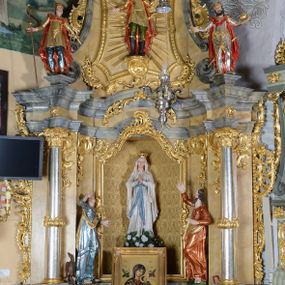 Zdjęcie nr 1: Nastawa ołtarzowa architektoniczna, jednoosiowa, jednokondygnacyjna ze zwieńczeniem. Ołtarz drewniany, prostopadłościenny, mensa drewniana z kamiennym portatylem. Antepedium w kształcie leżącego prostokąta, ujętego profilowaną ramą z aplikowanym monogramem Maryii w polu. Na ołtarzu ustawiony obraz Matki Boskiej Nieustającej Pomocy. Retabulum ustawione na dwustrefowym cokole, ujęte parą kolumn o kapitelach kompozytowych, przewiązanych poniżej połowy rocaille'ową opaską, stojących na tle zwielokrotnionych pilastrów. Podpory dźwigają pełne belkowanie, wyłamane na ich osi, ustawione ukośnie, nad polem środkowym przyjmujące kształt łuku odcinkowego. W polu środkowym głęboka nisza w formie stojącego prostokąta zamkniętego łukiem wklęsło-wypukłym z uskokami, ujęta profilowaną ramą, z figurą Matki Boskiej z Lourdes. Niszę flankują dwie figury: św. Jana i św. Mateusza ustawione na konsolach. Na belkowaniu, na linii podpór cokoły z figurami św. Emeryka i św. Władysława. Zwieńczenie przyjmuje kształt stojącego prostokąta flankowanego spływami wolutowymi, zamkniętego gzymsem przechodzącym w dwie woluty. Całość zakończona promienistą glorią z monogramem Marii otoczonym obłokami, flankowana figurkami aniołków. W polu zwieńczenia rama w formie stojącego prostokąta o wklęsłych bokach i dolnych narożach, zamknięta wolutami, z figurą św. Stefana w polu, ustawioną na wsporniku. Nastawa ujęta po bokach ażurowymi uszami utworzonymi z rocaille'u i prostej karbowanej wstęgi. Całość obficie dekorowana ornamentem rocaille'owym oraz zwisami kwiatowymi. Struktura marmoryzowana w kolorze żółtym, profile marmoryzowane na seledynowo, ornamentyka i profilowania złocone.

