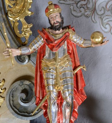 Zdjęcie nr 1: Rzeźba ścięta z tyłu, drążona, przedstawia św. Władysława. Figura stojąca w delikatnym kontrapoście, z rękoma rozchylonymi na boki, w lewej dłoni trzyma jabłko królewskie, w prawej berło. Twarz pociągła, okolona krótką brodą, nos długi i prosty, oczy skierowane ku górze. Włosy długie, kręcone, opadające na plecy, na głowie korona zamknięta. Święty jest ubrany w pełną zbroję płytową, ze złoconą szarfą przewiązaną na biodrach oraz złocony płaszcz, zapięty na lewym ramieniu, opadający na plecy, z tyłu zawieszona szabla. Polichromia naturalistyczna w odsłoniętych partiach ciała, zbroja srebrzona, detal złocony.