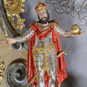 Zdjęcie nr 1: Rzeźba ścięta z tyłu, drążona, przedstawia św. Władysława. Figura stojąca w delikatnym kontrapoście, z rękoma rozchylonymi na boki, w lewej dłoni trzyma jabłko królewskie, w prawej berło. Twarz pociągła, okolona krótką brodą, nos długi i prosty, oczy skierowane ku górze. Włosy długie, kręcone, opadające na plecy, na głowie korona zamknięta. Święty jest ubrany w pełną zbroję płytową, ze złoconą szarfą przewiązaną na biodrach oraz złocony płaszcz, zapięty na lewym ramieniu, opadający na plecy, z tyłu zawieszona szabla. Polichromia naturalistyczna w odsłoniętych partiach ciała, zbroja srebrzona, detal złocony.