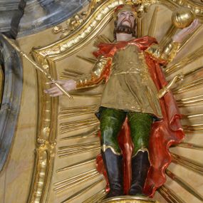 Zdjęcie nr 1: Rzeźba ścięta z tyłu, drążona, przedstawia św. Stefana. Figura ustawiona frontalnie, w delikatnym kontrapoście, z głową skierowaną ku górze. Ręce rozłożone na boki, w lewej dłoni trzyma jabłko królewskie, w prawej berło. Twarz pociągła, szczupła, okolona krótkim zarostem, z rozchylonymi ustami. Włosy krótkie, kręcone, na głowie zamknięta korona. Święty jest ubrany w buty z wysokimi cholewami, zielone spodnie oraz złocony kaftan z dekoracyjnym pasem w talii oraz czerwony płaszcz spięty na piersi broszą. Z tyłu ma zawieszony miecz, którego rękojeść jest wyrzeźbiona w kształcie głowy ptaka. Polichromia naturalistyczna w odsłoniętych partiach ciała, strój i atrybuty złocone.