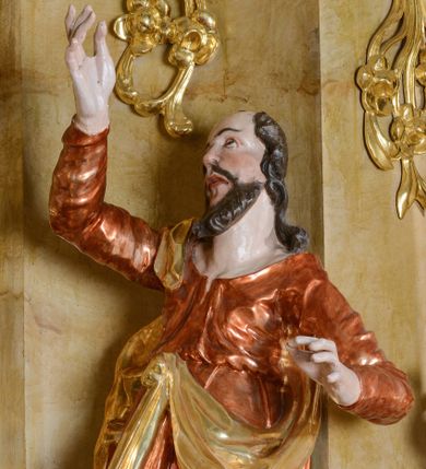 Zdjęcie nr 1: Rzeźba św. Mateusza ścięta z tyłu, drążona, ustawiona na półokrągłej podstawie. Figura ustawiona w silnym kontrapoście, delikatnie przechylona w tył, głowa skierowana ku górze. Prawa ręka wysoko uniesiona; lewa, ugięta, wyciągnięta w bok. Twarz pociągła, szczupła, z wysokim czołem, oczy skierowane do góry, mały nos, pełne usta; okolona krótką i kręcona brodą. Włosy długie, kręcone, opadające na ramiona. Święty jest ubrany w długą, jasnobrązową suknię z długimi rękawami, z dużym dekoltem, przepasaną w talii (tkanina marszczona w partii torsu, u dołu drapowana w grube fałdy) oraz złoty płaszcz zawieszony na prawym ramieniu, opadający na plecy z jedną połą zawieszoną u pasa. Polichromia naturalistyczna w odsłoniętych partiach ciała, szata laserunkowa, płaszcz złocony.