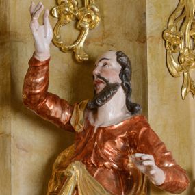 Zdjęcie nr 1: Rzeźba św. Mateusza ścięta z tyłu, drążona, ustawiona na półokrągłej podstawie. Figura ustawiona w silnym kontrapoście, delikatnie przechylona w tył, głowa skierowana ku górze. Prawa ręka wysoko uniesiona; lewa, ugięta, wyciągnięta w bok. Twarz pociągła, szczupła, z wysokim czołem, oczy skierowane do góry, mały nos, pełne usta; okolona krótką i kręcona brodą. Włosy długie, kręcone, opadające na ramiona. Święty jest ubrany w długą, jasnobrązową suknię z długimi rękawami, z dużym dekoltem, przepasaną w talii (tkanina marszczona w partii torsu, u dołu drapowana w grube fałdy) oraz złoty płaszcz zawieszony na prawym ramieniu, opadający na plecy z jedną połą zawieszoną u pasa. Polichromia naturalistyczna w odsłoniętych partiach ciała, szata laserunkowa, płaszcz złocony.