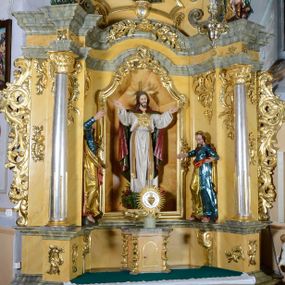 Zdjęcie nr 1: Nastawa ołtarzowa architektoniczna, jednoosiowa, jednokondygnacyjna ze zwieńczeniem. Ołtarz drewniany, prostopadłościenny, mensa drewniana z kamiennym portatylem. Antepedium w kształcie leżącego prostokąta, ujętego profilowaną ramą. Na ołtarzu tabernakulum w formie prostopadłościennej skrzynki, ujętej w narożach pilastrami o ornamentalnych trzonach, dźwigających pełne belkowanie opasujące tabernakulum z trzech stron, wyłamane na ich osi. Drzwiczki w formie stojącego prostokąta zamkniętego łukiem nadwieszonym. Retabulum ustawione na dwustrefowym cokole, ujęte parą kolumn o kapitelach kompozytowych, stojących na tle zwielokrotnionych pilastrów. Podpory dźwigają pełne belkowanie, wyłamane na ich osi, ustawione ukośnie, nad polem środkowym przyjmujące kształt łuku odcinkowego. W polu środkowym głęboka nisza w formie stojącego prostokąta zamkniętego łukiem wklęsło-wypukłym z uskokami, ujęta profilowaną ramą, z figurą Najświętszego Serca Jezusa. Niszę flankują dwie figury: św. Marka i św. Łukasza ustawione na konsolach. Na belkowaniu, na linii podpór cokoły z figurami św. Alojzego Gonzagi i św. Rocha. Zwieńczenie przyjmuje kształt stojącego prostokąta flankowanego spływami wolutowymi, zamkniętego gzymsem przechodzącym w dwie woluty. Całość zakończona owalnym medalionem z płaskorzeźbionym przedstawieniem Trójcy Świętej w promienistej glorii, flankowana figurkami św. Katarzyny Aleksandryjskiej i nierozpoznanej świętej. W polu zwieńczenia rama w formie stojącego prostokąta o wklęsłych bokach i dolnych narożach, zamknięta wolutami z akroterionem, z figurą św. Sebastiana w polu, ustawioną na wsporniku. Nastawa ujęta po bokach ażurowymi uszami utworzonymi z akantu i prostej karbowanej wstęgi. Całość obficie dekorowana ornamentem rocaille'owym oraz zwisami kwiatowymi. Struktura marmoryzowana w kolorze żółtym, profile marmoryzowane na seledynowo, ornamentyka i profilowania złocone.