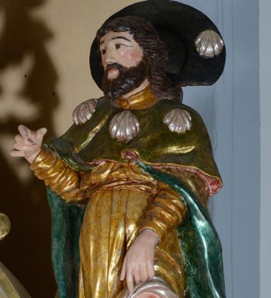 Zdjęcie nr 1: Rzeźba pełnoplastyczna przedstawiająca św. Rocha. Figura ustawiona w kontrapoście z lewą nogą wysuniętą do przodu. Prawa ręka ugięta w łokciu, lewa opuszczona w dół wskazuje na ranę na nodze. Twarz szeroka, z małymi ustami, długim i prostym nosem, podłużnymi oczami okolonymi wąskimi łukami brwiowymi; broda krótka i gęsta; włosy sięgające do ramion, zawinięte do tyłu w bujne loki. Święty jest ubrany w złoconą suknię ze srebrną podszewką i długimi rękawami, podwiniętą u dołu i odsłaniającą lewą nogę oraz zielony płaszcz pielgrzymi z turkusową podszewką, zdobiony u góry trzema muszlami. Na szyi zawieszony za plecami czarny kapelusz pielgrzymi z jedną muszlą. U stóp świętego pies z kawałkiem chleba w pysku. Polichromia w odsłoniętych partiach ciała naturalistyczna, szaty złocone, detale srebrzone.