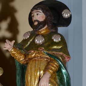 Zdjęcie nr 1: Rzeźba pełnoplastyczna przedstawiająca św. Rocha. Figura ustawiona w kontrapoście z lewą nogą wysuniętą do przodu. Prawa ręka ugięta w łokciu, lewa opuszczona w dół wskazuje na ranę na nodze. Twarz szeroka, z małymi ustami, długim i prostym nosem, podłużnymi oczami okolonymi wąskimi łukami brwiowymi; broda krótka i gęsta; włosy sięgające do ramion, zawinięte do tyłu w bujne loki. Święty jest ubrany w złoconą suknię ze srebrną podszewką i długimi rękawami, podwiniętą u dołu i odsłaniającą lewą nogę oraz zielony płaszcz pielgrzymi z turkusową podszewką, zdobiony u góry trzema muszlami. Na szyi zawieszony za plecami czarny kapelusz pielgrzymi z jedną muszlą. U stóp świętego pies z kawałkiem chleba w pysku. Polichromia w odsłoniętych partiach ciała naturalistyczna, szaty złocone, detale srebrzone.