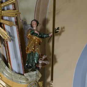 Zdjęcie nr 1: Rzeźba pełnoplastyczna przedstawiająca św. Katarzynę Aleksandryjską. Święta stoi na niskim cokole, prawą rękę ma złożoną na piersi, w lewej odsuniętej w bok trzyma palmę męczeństwa, głowę ma skierowaną w prawo. Twarz owalna o delikatnych rysach, z długim i prostym nosem, bardzo małymi ustami, okolona bujnymi włosami, zasłaniającymi uszy i podwiniętymi do tyłu w bujne fale, policzki intensywnie zarumienione. Święta jest ubrana w zieloną, długą suknię z długimi rękawami oraz złocony płaszcz założony na prawe ramię i otulający postać z przodu, na stopach ma czarne buty. Po lewej stronie świętej koło – narzędzie jej męczeństwa. Polichromia w odsłoniętych partiach ciała naturalistyczna, jasna.

