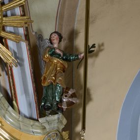 Zdjęcie nr 1: Rzeźba pełnoplastyczna przedstawiająca św. Katarzynę Aleksandryjską. Święta stoi na niskim cokole, prawą rękę ma złożoną na piersi, w lewej odsuniętej w bok trzyma palmę męczeństwa, głowę ma skierowaną w prawo. Twarz owalna o delikatnych rysach, z długim i prostym nosem, bardzo małymi ustami, okolona bujnymi włosami, zasłaniającymi uszy i podwiniętymi do tyłu w bujne fale, policzki intensywnie zarumienione. Święta jest ubrana w zieloną, długą suknię z długimi rękawami oraz złocony płaszcz założony na prawe ramię i otulający postać z przodu, na stopach ma czarne buty. Po lewej stronie świętej koło – narzędzie jej męczeństwa. Polichromia w odsłoniętych partiach ciała naturalistyczna, jasna.

