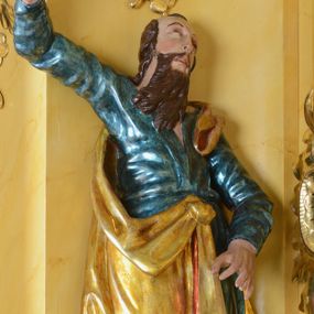 Zdjęcie nr 1: Rzeźba św. Marka ścięta z tyłu, ustawiona na niskim półokrągłym cokole. Figura ukazana w delikatnym kontrapoście z prawą nogą ugiętą w kolanie i wysuniętą do przodu, z prawą ręką uniesioną wysoko, a lewą ugiętą w łokciu i opuszczoną w dół, dłonie masywne. Święty ma głowę zwróconą ku górze i przechyloną delikatnie w lewo. Twarz podłużna, okolona długą i bujną brodą oraz średniej długości włosami opadającymi na plecy i zasłaniającymi uszy; nos długi i wąski, usta otwarte, oczy skierowane ku górze. Święty ubrany jest w niebieską suknię z długimi rękawami, przepasaną w talii oraz zarzucony na lewe ramię złoty płaszcz z czerwoną podszewką, opadający na plecy, z jedną połą upiętą na brzuchu. Tkanina sztywna, drapowana w grube fałdy. U stóp świętego głowa lwa. Polichromia w odsłoniętych partiach ciała naturalistyczna, płaszcz złocony.