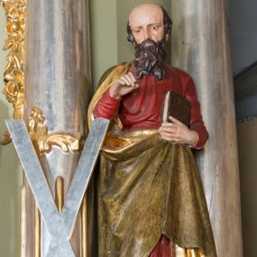 Zdjęcie nr 1: Rzeźba św. Andrzeja ścięta z tyłu, ustawiona na niskim, prostopadłościennym cokole o ściętych narożach. Figura zwrócona frontalnie, z prawą nogą delikatnie ugiętą w kolanie, z pochyloną głową. Lewą ręką przytrzymuje przy piersi zamkniętą księgę; prawą również ugiętą, unosi przed siebie. Twarz o wysokim czole, z wyraźnie zaznaczoną łysiną okolona długą, falującą brodą, rozdzieloną na końcu na dwa pukle, nos długi i wąski, oczy skierowane w dół. Włosy średniej długości, widoczne po bokach głowy. Święty jest ubrany w czerwoną suknię z długimi rękawami oraz  płaszcz w kolorze brudnozłotym ze złoconą podszewką, zawieszony na prawym ramieniu i podtrzymywany z przodu, drapowany w grube, miękkie fałdy. Obok rzeźby, po lewej stronie stoi wysoki, srebrzony krzyż w kształcie litery „X”. Polichromia w odsłoniętych partiach ciała naturalistyczna, podszewka płaszcza złocona, krzyż srebrzony.