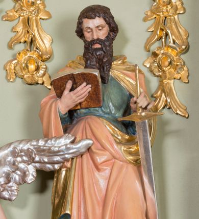 Zdjęcie nr 1: Rzeźba ścięta z tyłu, ustawiona na niskim cokole o ściętych z przodu narożach. Święty ustawiony frontalnie w postawie stojącej, w dużym kontrapoście z lewą nogą ugiętą w kolanie, z otwartą księgą w prawej dłoni oraz mieczem w lewej, ostrzem skierowanym w dół. Głowa skierowana w stronę księgi, twarz podłużna, nos długi i szeroki, oczy delikatnie przymknięte. Włosy ciemnobrązowe, średniej długości, zasłaniające uszy; broda długa i bujna. Święty jest ubrany w niebieską suknię, przewiązaną w talii oraz różowy płaszcz ze złotą podszewką i kapturem, na stopach sandały. Polichromia w odsłoniętych partiach ciała naturalistyczna, podbicie płaszcza złocone, ostrze miecza srebrzone.