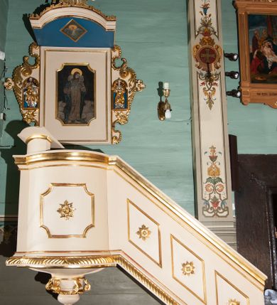 Zdjęcie nr 1: Ambona wisząca, przyścienna, złożona z kosza i schodów z balustradą, zaplecka i baldachimu ze zwieńczeniem. Kosz na planie kwadratu z wypukłą ścianą frontową, ujęty jednym pilastrem przy ścianie bocznej. Na ścianach płyciny o wykroju kwadratu z wklęsłymi narożami, wewnątrz rozety. Kosz zakończony profilowanym gzymsem, od dołu otoczony pasem z dekoracją w formie nacięć. Spięty u dołu szyszką z fryzem zdobionym czterema wolutami oraz pierścieniem z dekoracją w formie łezek. Od wschodu schody jednobiegowe z balustradą zdobioną płycinami z rozetami oraz profilowaną poręczą. Pulpit w kształcie kwadratu zamkniętego łukiem odcinkowym nadwieszonym. Zaplecek w formie stojącego prostokąta, ujęty uszami utworzonymi z ornamentu rocaille’owego połączonego z wicią i rozetami, z umieszczonymi w strukturze płaskorzeźbami postaci w niszach zamkniętych łukiem półokrągłym i wypełnionych muszlą; po lewej Jezus z barankiem, po prawej św. Kazimierz (?). Pośrodku pole obrazowe o wykroju stojącego prostokąta z wklęsłymi narożami, w nim obraz Chrystusa Dobrego Pasterza. Baldachim w formie prostokąta zamkniętego od zewnętrznej strony łukiem odcinkowym nadwieszonym; podniebie malowane na niebiesko, pośrodku pole obrazowe w formie rombu, wypełnione przedstawieniem gołębicy Ducha Świętego. Ponad baldachimem duża gloria promienista, w centrum której wizerunek Oka Opatrzności.