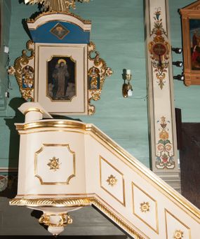 Zdjęcie nr 1: Ambona wisząca, przyścienna, złożona z kosza i schodów z balustradą, zaplecka i baldachimu ze zwieńczeniem. Kosz na planie kwadratu z wypukłą ścianą frontową, ujęty jednym pilastrem przy ścianie bocznej. Na ścianach płyciny o wykroju kwadratu z wklęsłymi narożami, wewnątrz rozety. Kosz zakończony profilowanym gzymsem, od dołu otoczony pasem z dekoracją w formie nacięć. Spięty u dołu szyszką z fryzem zdobionym czterema wolutami oraz pierścieniem z dekoracją w formie łezek. Od wschodu schody jednobiegowe z balustradą zdobioną płycinami z rozetami oraz profilowaną poręczą. Pulpit w kształcie kwadratu zamkniętego łukiem odcinkowym nadwieszonym. Zaplecek w formie stojącego prostokąta, ujęty uszami utworzonymi z ornamentu rocaille’owego połączonego z wicią i rozetami, z umieszczonymi w strukturze płaskorzeźbami postaci w niszach zamkniętych łukiem półokrągłym i wypełnionych muszlą; po lewej Jezus z barankiem, po prawej św. Kazimierz (?). Pośrodku pole obrazowe o wykroju stojącego prostokąta z wklęsłymi narożami, w nim obraz Chrystusa Dobrego Pasterza. Baldachim w formie prostokąta zamkniętego od zewnętrznej strony łukiem odcinkowym nadwieszonym; podniebie malowane na niebiesko, pośrodku pole obrazowe w formie rombu, wypełnione przedstawieniem gołębicy Ducha Świętego. Ponad baldachimem duża gloria promienista, w centrum której wizerunek Oka Opatrzności.