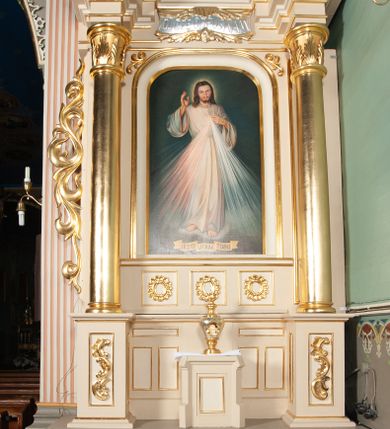 Zdjęcie nr 3: Obraz w kształcie pionowego owalu. W centrum św. Teresa ukazana frontalnie, w półpostaci, z głową lekko zwróconą na lewo. W uniesionych przed sobą dłoniach trzyma białe i jasnoróżowe róże oraz niewielki krucyfiks. Ubrana jest w strój karmelitański: brązowy habit i jasny płaszcz, białą tokę oraz czarny welon. Jej głowę otacza nimb. Tło jest jednolite, ciemnobrązowe, z prawej strony widać padające skośnie promienie. Obraz został umieszczony w profilowanej, drewnianej, złoconej ramie w zwieńczeniu ołtarza bocznego.