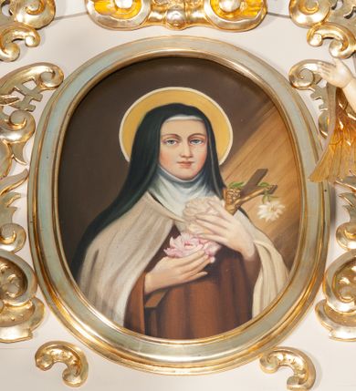 Zdjęcie nr 1: Obraz w kształcie pionowego owalu. W centrum św. Teresa ukazana frontalnie, w półpostaci, z głową lekko zwróconą na lewo. W uniesionych przed sobą dłoniach trzyma białe i jasnoróżowe róże oraz niewielki krucyfiks. Ubrana jest w strój karmelitański: brązowy habit i jasny płaszcz, białą tokę oraz czarny welon. Jej głowę otacza nimb. Tło jest jednolite, ciemnobrązowe, z prawej strony widać padające skośnie promienie. Obraz został umieszczony w profilowanej, drewnianej, złoconej ramie w zwieńczeniu ołtarza bocznego.