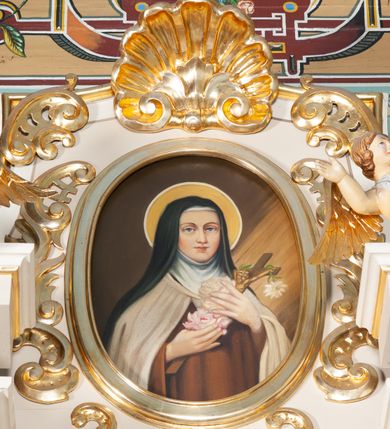 Zdjęcie nr 4: Ołtarz architektoniczny, przyścienny, jednoosiowy, jednokondygnacyjny ze zwieńczeniem. Nastawa umieszczona jest na skrzyniowej mensie z kamiennym blatem. Antepedium ozdabia okrągła płycina z czteroliściem wpisanym w koło, flankowana przez dwie kwadratowe płyciny, których wewnętrzne krawędzie są wklęsłe. Boczne ścianki mensy ozdobione są prostokątną płyciną. Nastawa flankowana ustawionymi na wysuniętych partiach cokołu kolumnami dźwigającymi pełne belkowanie wyłamane na ich osiach i podtrzymujące fragmenty urwanego przyczółka. Cokół jest dekorowany prostokątnymi płycinami, na osiach zewnętrznych dodatkowo wypełnionymi ornamentem małżowinowym i rocaille’owym. W polu centralnym nisza zamknięta od góry łukiem spłaszczonym, w której na tle złoconego tła umieszczono krucyfiks przesłaniany wizerunkiem „Jezu Ufam Tobie”. Poniżej niszy trzy płyciny z symetryczną dekoracją rocaille’ową, powyżej wstęga z napisem „OJCZĘ ODPUS NAM” ujęta liśćmi. Kondygnacja jest z lewej strony ujęta uszakiem skomponowanym z ażurowej wici akantowej. Pole zwieńczenia wypełnia rama w kształcie stojącego owalu z wizerunkiem św. Teresy od Dzieciątka Jezus otoczona ornamentem inspirowanym małżowinowym. Powyżej muszla palmetowa, na urwanych fragmentach przyczółka posadowiono anioły. 
Struktura polichromowana na kremowo ze złoconą i srebrzoną ornamentyką oraz detalami architektonicznymi. 