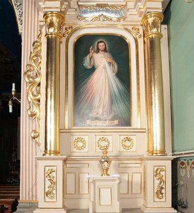 Zdjęcie nr 1: Ołtarz architektoniczny, przyścienny, jednoosiowy, jednokondygnacyjny ze zwieńczeniem. Nastawa umieszczona jest na skrzyniowej mensie z kamiennym blatem. Antepedium ozdabia okrągła płycina z czteroliściem wpisanym w koło, flankowana przez dwie kwadratowe płyciny, których wewnętrzne krawędzie są wklęsłe. Boczne ścianki mensy ozdobione są prostokątną płyciną. Nastawa flankowana ustawionymi na wysuniętych partiach cokołu kolumnami dźwigającymi pełne belkowanie wyłamane na ich osiach i podtrzymujące fragmenty urwanego przyczółka. Cokół jest dekorowany prostokątnymi płycinami, na osiach zewnętrznych dodatkowo wypełnionymi ornamentem małżowinowym i rocaille’owym. W polu centralnym nisza zamknięta od góry łukiem spłaszczonym, w której na tle złoconego tła umieszczono krucyfiks przesłaniany wizerunkiem „Jezu Ufam Tobie”. Poniżej niszy trzy płyciny z symetryczną dekoracją rocaille’ową, powyżej wstęga z napisem „OJCZĘ ODPUS NAM” ujęta liśćmi. Kondygnacja jest z lewej strony ujęta uszakiem skomponowanym z ażurowej wici akantowej. Pole zwieńczenia wypełnia rama w kształcie stojącego owalu z wizerunkiem św. Teresy od Dzieciątka Jezus otoczona ornamentem inspirowanym małżowinowym. Powyżej muszla palmetowa, na urwanych fragmentach przyczółka posadowiono anioły. 
Struktura polichromowana na kremowo ze złoconą i srebrzoną ornamentyką oraz detalami architektonicznymi. 