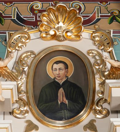 Zdjęcie nr 2: Ołtarz architektoniczny, przyścienny, jednoosiowy, jednokondygnacyjny ze zwieńczeniem. Nastawa umieszczona jest na skrzyniowej mensie z kamiennym blatem. Antepedium ozdabia okrągła płycina z otaczającym monogram IHS czteroliściem wpisanym w koło, flankowana przez dwie kwadratowe płyciny, których wewnętrzne krawędzie są wklęsłe. Boczne ścianki mensy ozdobione są prostokątną płyciną. Nastawa flankowana ustawionymi na wysuniętych partiach cokołu kolumnami dźwigającymi pełne belkowanie wyłamane na ich osiach i podtrzymujące fragmenty urwanego przyczółka. Cokół jest dekorowany prostokątnymi płycinami, na osiach zewnętrznych dodatkowo wypełnionymi ornamentem małżowinowym i rocaille’owym. W polu centralnym nisza zamknięta od góry łukiem spłaszczonym, w której znajduje się wizerunek św. Józefa z małym Jezusem. Poniżej niszy trzy płyciny z symetryczną dekoracją rocaille’ową, powyżej wstęga z napisem „BÓG UWIELBIONY I BŁ[OGOSŁAWIONY]” ujęta liśćmi. Kondygnacja jest z prawej strony ujęta uszakiem skomponowanym z ażurowej wici akantowej. Pole zwieńczenia wypełnia rama w kształcie stojącego owalu z wizerunkiem św. Stanisława Kostki, otoczona ornamentem inspirowanym małżowinowym. Powyżej muszla palmetowa, a na urwanych fragmentach przyczółka posadowiono anioły. 
Struktura polichromowana na kremowo ze złoconą i srebrzoną ornamentyką oraz detalami architektonicznymi.