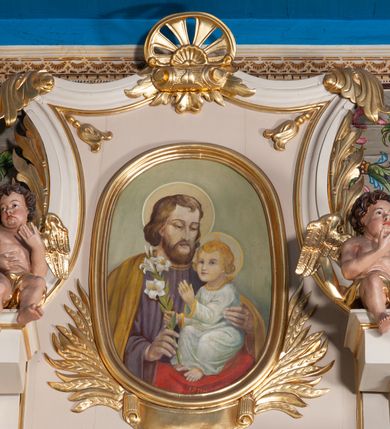 Zdjęcie nr 6: Ołtarz przyścienny, architektoniczny, na cokole. Mensa drewniana. Antepedium w kształcie leżącego prostokąta, ujęte profilami, z okrągłą plakietą z monogramem IHS po środku. Na mensie tabernakulum na rzucie prostokąta z uskokiem, dekorowane płycinami w kształcie stojących prostokątów, z drzwiczkami ozdabianymi aplikowanym kielichem z hostią. Nastawa jednoosiowa, jednokondygnacyjna ze zwieńczeniem. Oś środkowa flankowana parą kręconych kolumn o kapitelach kompozytowych ustawionych przed licem, na tle pilastrów. Podpory dźwigają pełne, wyłamane belkowanie oraz odpowiadający ich ułożeniu przerwany przyczółek. Zwieńczenie ujęte w spływy, zamknięte łukiem kotarowym dwudzielnym. Cokoły kolumn dekorowane plakietami z ornamentem roślinnym. W polu środkowym obraz we wnęce z przedstawieniem Najświętszego Serca Jezusa w profilowanej ramie, w formie stojącego prostokąta, powyżej puste pole kartusza. Pierwsza kondygnacja ujęta z prawej strony uszakiem utworzonym z wici roślinnej. Na przerwanym przyczółku spoczywa para aniołów. W zwieńczeniu profilowana owalna rama z obrazem św. Józefa powyżej kartusza i wśród kłosów zbóż, spływy ujmujące zwieńczenie dekorują liście. 
Struktura polichromowana na kremowo ze złoconą i srebrzoną ornamentyką oraz detalami architektonicznymi.