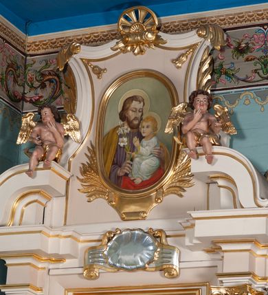 Zdjęcie nr 5: Ołtarz przyścienny, architektoniczny, na cokole. Mensa drewniana. Antepedium w kształcie leżącego prostokąta, ujęte profilami, z okrągłą plakietą z monogramem IHS po środku. Na mensie tabernakulum na rzucie prostokąta z uskokiem, dekorowane płycinami w kształcie stojących prostokątów, z drzwiczkami ozdabianymi aplikowanym kielichem z hostią. Nastawa jednoosiowa, jednokondygnacyjna ze zwieńczeniem. Oś środkowa flankowana parą kręconych kolumn o kapitelach kompozytowych ustawionych przed licem, na tle pilastrów. Podpory dźwigają pełne, wyłamane belkowanie oraz odpowiadający ich ułożeniu przerwany przyczółek. Zwieńczenie ujęte w spływy, zamknięte łukiem kotarowym dwudzielnym. Cokoły kolumn dekorowane plakietami z ornamentem roślinnym. W polu środkowym obraz we wnęce z przedstawieniem Najświętszego Serca Jezusa w profilowanej ramie, w formie stojącego prostokąta, powyżej puste pole kartusza. Pierwsza kondygnacja ujęta z prawej strony uszakiem utworzonym z wici roślinnej. Na przerwanym przyczółku spoczywa para aniołów. W zwieńczeniu profilowana owalna rama z obrazem św. Józefa powyżej kartusza i wśród kłosów zbóż, spływy ujmujące zwieńczenie dekorują liście. 
Struktura polichromowana na kremowo ze złoconą i srebrzoną ornamentyką oraz detalami architektonicznymi.