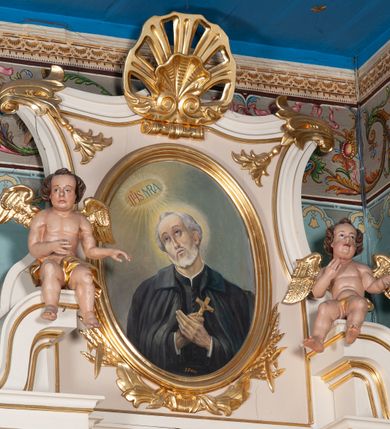 Zdjęcie nr 17: Ołtarz przyścienny, architektoniczny, na cokole. Mensa drewniana. Antepedium w kształcie leżącego prostokąta, wypełnione płyciną, z monogramem maryjnym pośrodku. Na mensie tabernakulum w na rzucie trapezu, z drzwiczkami w kształcie stojącego prostokąta zamkniętego półkoliście dekorowanymi aplikowanym kielichem z hostią. Nastawa ołtarzowa jednoosiowa, jednokondygnacyjna ze zwieńczeniem. Oś środkowa flankowana parą kręconych kolumn o kapitelach kompozytowych ustawionych przed licem, na tle pilastrów. Podpory dźwigają pełne, wyłamane belkowanie oraz odpowiadający ich ułożeniu przerwany przyczółek. Zwieńczenie ujęte w spływy, zamknięte łukiem kotarowym dwudzielnym spiętym muszlą palmetową. Cokoły kolumn dekorowane plakietami z ornamentem roślinnym. W polu środkowym obraz we wnęce z przedstawieniem Matki Boskiej Różańcowej w profilowanej ramie, w formie stojącego prostokąta zamkniętego półkoliście, powyżej puste pole kartusza. Pierwsza kondygnacja ujęta z lewej strony uszakiem utworzonym z wici roślinnej. Na przerwanym przyczółku spoczywa para aniołków. W zwieńczeniu profilowana owalna rama z obrazem św. Andrzeja Boboli otoczona od dołu kłosami zbóż. 
Struktura polichromowana na kremowo ze złoconą i srebrzoną ornamentyką oraz detalami architektonicznymi.
