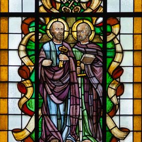 Zdjęcie nr 1: Witraż w formie stojącego prostokąta zwieńczonego łukiem trójwklęsłym. Przedstawia wizerunek św. Piotra i św. Pawła, ukazanych frontalnie, całopostaciowo. Po lewej stronie kompozycji św. Piotr z kluczem w lewej dłoni, prawą unosi zaciśniętą. Jest ubrany w niebiesko-zieloną suknię i bordowy płaszcz przerzucony przez ręce i lewe ramię. Po prawej św. Paweł z księgą w lewej i opartym o ziemię mieczem w prawej ręce. Ma na sobie zieloną suknię i bordowy płaszcz owinięty wokół szyi i lewej ręki. Powyżej świętych tiara papieska ze skrzyżowanymi poniżej kluczami. Wizerunek ujęty zielonymi polami o nieregularnym kształcie i stylizowanymi wstęgami. Całość przedstawienia na tle pól z niebarwionego szkła. Wzdłuż dłuższych boków witraża i łuku bordiura w postaci ciemnożółtej wstęgi. U stóp świętych inskrypcja „ŚW(IĘTEMU) PIOTROWI / i PAWŁOWI / WITRAŻ OFIAROWA/ŁA  GROMADA / OCHODZA / R[OKU] P[AŃSKIEGO] 1953”. Witraż o intensywnych kolorach, z przewagą bordowego i zielonego. 