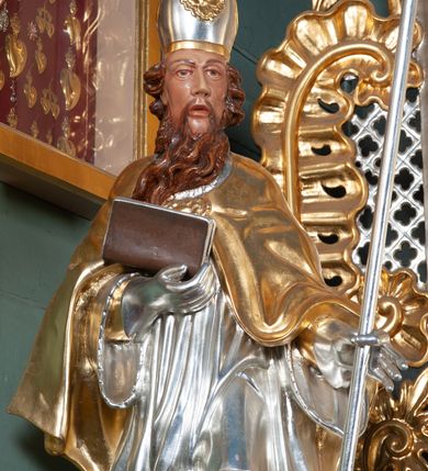 Zdjęcie nr 5: Ołtarz przyścienny, architektoniczny, na cokole, z bramkami. Nastawa jednoosiowa, jednokondygnacyjna ze zwieńczeniem. Mensa murowana, blat kamienny. Antepedium w kształcie leżącego prostokąta ujętego parami kolumn o gładkich trzonach i głowicach kompozytowych, podtrzymujących belkowanie z parami tryglifów. Belkowanie nad częścią środkową ucięte łukowato. W polu środkowym płaskorzeźbiona scena z przedstawieniem Świętej Rodziny. Postać św. Józefa półleżąca, zwrócona profilem w prawo, w stronę Matki Boskiej. Siedząca Maria skierowana w trzech czwartych w prawo, trzyma na kolanach poruszone Dzieciątko. Oś środkowa flankowana parą opilastrowanych filarów i kolumn o kapitelach kompozytowych, ustawionych przed licem ołtarza pod kątem. Podpory dźwigają pełne, wyłamane belkowanie oraz odpowiadający ich ułożeniu przerwany przyczółek. Zwieńczenie ujęte w spływy, zamknięte łukiem nadwieszonym. Cokoły kolumn dekorowane rocaille’em. W polu środkowym obraz we wnęce z przedstawieniem Matki Boskiej z Dzieciątkiem zasłaniany wizerunkiem św. Floriana w profilowanej ramie, w formie stojącego prostokąta zamkniętego dwoma, zwróconymi naprzeciwlegle stykającymi się spływami wolutowymi oraz rocaille’owym kartuszem z inskrypcją „POD TWOJĄ OBRONĘ”. Pierwsza kondygnacja ujęta uszakami utworzonymi z ornamentu rocaille’owego, ażurowej kratki regencyjnej i ornamentu roślinnego w formie kwiatów. Na bramkach ustawiono figury św. Wojciecha i św. Stanisława. Na przerwanym przyczółku spoczywa para adorujących aniołów. W zwieńczeniu profilowana rama powtarzająca jego formę z obrazem św. Antoniego Padewskiego zamknięta rocaille’em. Całość ujęta w spływy z ornamentu roślinnego. Struktura polichromowana na kremowo ze złoconą i srebrzoną ornamentyką oraz detalami architektonicznymi.