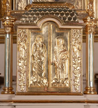 Zdjęcie nr 1: Tabernakulum w kształcie domku na podwójnym cokole, zwieńczonego dachem mansardowym, pokrytym dachówkami w formie łusek, z chwostami na krańcach kalenicy. Drzwiczki w kształcie stojącego prostokąta zakończonego łukiem nadwieszonym z płaskorzeźbionymi wizerunkami św. Piotra po lewej stronie i św. Pawła po prawej i aniołami na rewersie. Święci mają wydłużone proporcje i są ciasno owinięci płaszczami. Drzwiczki ujęte lizenami z dekoracją w formie festonów utworzonych z wstęgi regencyjnej, winnej latorośli i ornamentu roślinnego. 
Całość flankowana przez dwie wolnostojące kolumny o kanelowanych trzonach oraz kapitelach dekorowanych akantem i jajownikiem, dźwigających echinus z wazonem. 
Tabernakulum polichromowane na kremowo ze złoconymi drzwiczkami, dachem i kolumnami.