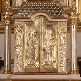 Zdjęcie nr 1: Tabernakulum w kształcie domku na podwójnym cokole, zwieńczonego dachem mansardowym, pokrytym dachówkami w formie łusek, z chwostami na krańcach kalenicy. Drzwiczki w kształcie stojącego prostokąta zakończonego łukiem nadwieszonym z płaskorzeźbionymi wizerunkami św. Piotra po lewej stronie i św. Pawła po prawej i aniołami na rewersie. Święci mają wydłużone proporcje i są ciasno owinięci płaszczami. Drzwiczki ujęte lizenami z dekoracją w formie festonów utworzonych z wstęgi regencyjnej, winnej latorośli i ornamentu roślinnego. 
Całość flankowana przez dwie wolnostojące kolumny o kanelowanych trzonach oraz kapitelach dekorowanych akantem i jajownikiem, dźwigających echinus z wazonem. 
Tabernakulum polichromowane na kremowo ze złoconymi drzwiczkami, dachem i kolumnami.