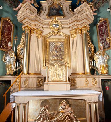 Zdjęcie nr 3: Tabernakulum w kształcie domku na podwójnym cokole, zwieńczonego dachem mansardowym, pokrytym dachówkami w formie łusek, z chwostami na krańcach kalenicy. Drzwiczki w kształcie stojącego prostokąta zakończonego łukiem nadwieszonym z płaskorzeźbionymi wizerunkami św. Piotra po lewej stronie i św. Pawła po prawej i aniołami na rewersie. Święci mają wydłużone proporcje i są ciasno owinięci płaszczami. Drzwiczki ujęte lizenami z dekoracją w formie festonów utworzonych z wstęgi regencyjnej, winnej latorośli i ornamentu roślinnego. 
Całość flankowana przez dwie wolnostojące kolumny o kanelowanych trzonach oraz kapitelach dekorowanych akantem i jajownikiem, dźwigających echinus z wazonem. 
Tabernakulum polichromowane na kremowo ze złoconymi drzwiczkami, dachem i kolumnami.