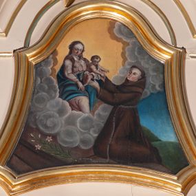 Zdjęcie nr 1: Pole obrazowe w kształcie wklęsło-wypukłym. W centrum scena, w której klęczący św. Antoni odbiera Dzieciątko Jezus od ukazującej mu się na obłokach Marii. Święty ma okrągłą twarz, wąski nos i rumieńce, na głowie wyciętą tonsurę, jest ubrany w brązowy habit franciszkański. Matka Boska siedzi, prawą rękę ma położoną na udzie, patrzy na rozgrywającą się scenę. Ma okrągłą twarz i długie włosy spływające na ramiona i plecy. Jest ubrana w różową suknię, niebieski płaszcz oraz zarzucony na głowę, przezroczysty welon. Dzieciątko wyciąga ręce w stronę św. Antoniego, jest przepasane białą tkaniną. U dołu sceny po lewej stronie leży kwiat lilii. Tło zróżnicowane: za Matką Boską żółte, za św. Antonim niebieskie, między nimi kłębią się szare obłoki, poniżej nich podest; silny światłocień. 