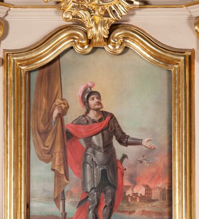 Zdjęcie nr 2: Pole obrazowe w formie stojącego prostokąta. W centrum kompozycji św. Florian ujęty całopostaciowo, ustawiony w trzech czwartych w lewo. Prawą ręką przytrzymuje ciemnożółtą chorągiew, lewą odwodzi do boku i spogląda w górę. Ma okrągłą twarz, wąski nos oraz pełne usta. Na plecy opadają mu jasne włosy, twarz okala jasnobrązowa, krótka broda. Jest ubrany w zakrywającą całe ciało zbroję, hełm z czerwonym pióropuszem oraz czerwony płaszcz, który dekoracyjnie przechodzi przez pierś, prawe ramię i opada przez plecy na ziemię, zahaczając o przytroczoną do biodra szablę. W tle płynie rzeka, a z prawej strony anioł gasi pożar trawiący miasteczko. Kolorystyka jasna, pastelowa. Subtelny światłocień. W prawym dolnym rogu sygnatura „GAŁKIEWICZ (?) / 1882 / KRAKÓW”.