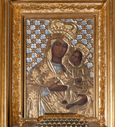 Zdjęcie nr 1: Obraz w kształcie stojącego prostokąta z przedstawieniem Marii ujętej w półfigurze, zwróconej nieznacznie w lewo, z Dzieciątkiem Jezus na lewej ręce. Maria lewą ręką wskazuje na Jezusa, prawą podtrzymuje jego nogi, patrzy na widza. Ma owalną twarz, brązowe oczy, wąski nos i małe, wydatne usta. Dzieciątko patrzy na Matkę, prawą ręką czyni gest błogosławieństwa, lewą przytrzymuje zamkniętą księgę. Ma owalną twarz, prosty nos i wąskie usta oraz krótkie, brązowe włosy. Karnacja obu postaci jest ciemna, światłocień delikatny. Resztę obrazu przykrywają srebrne, złocone sukienki oraz tło. Maria ubrana jest w srebrną suknię oraz złoty, przykrywający głowę płaszcz dekorowany rozwiniętymi kwiatami, spięty pod szyją. Dzieciątko ma na sobie długą, złotą, przewiązaną w pasie sukienkę. Oboje mają na głowach zamknięte korony. Tło dekorowane kratką, na przecięciu listewek rozetki. Obraz ujęty złotą ramą zdobioną wicią roślinną i rocaille’em. 