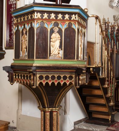 Zdjęcie nr 1: Ambona wolnostojąca, dostępna schodkami od strony prezbiterium, z pulpitem do czytania. Kosz sześcioboczny ustawiony na postumencie o przekroju wieloliścia utworzonym z wiązki kolumienek o złoconych bazach i trzonach zdobionych rytym ornamentem roślinnym, osadzonym na niskim, sześciobocznym cokole. U podstawy kosza ostrołukowy fryz arkadkowy. Ścianki kosza podzielone na trzy części dekoracją pseudomaswerkową w formie arkadek. W środkowej arkadce każdego z pól płaskorzeźbione, polichromowane i złocone przedstawienie ewangelistów:  św. Jana, św. Mateusza, św. Marka i św. Łukasza. Powyżej fryz ze stylizowanych lilii heraldycznych. Schody jednobiegowe, z balustradą utworzoną z rzędu wąskich kolumienek, ustawionych na niskich cokołach i bazach, o złoconych trzonach i półkolistych kapitelach. Każdy z ewangelistów ukazany całopostaciowo, frontalnie, z księgą w lewej ręce i piórem w prawej. U stóp ewangelistów przedstawiono odpowiadające im atrybuty: św. Marka – lew, św. Jana – orzeł, św. Mateusza – człowiek, św. Łukasza - wół. Ewangeliści, oprócz św. Jana mają rysy twarzy dojrzałych mężczyzn, z brodami, św. Jan bez brody z długimi i jasnymi włosami, opadającymi na plecy. Ubrani są w długie złocone suknie i złocone płaszcze. Struktura malowana na ciemny brąz, płyciny na kolor niebieski, zielony i czerwony, partie ornamentu złocone. 