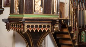 Zdjęcie nr 1: Ambona wolnostojąca, dostępna schodkami od strony prezbiterium, z pulpitem do czytania. Kosz sześcioboczny ustawiony na postumencie o przekroju wieloliścia utworzonym z wiązki kolumienek o złoconych bazach i trzonach zdobionych rytym ornamentem roślinnym, osadzonym na niskim, sześciobocznym cokole. U podstawy kosza ostrołukowy fryz arkadkowy. Ścianki kosza podzielone na trzy części dekoracją pseudomaswerkową w formie arkadek. W środkowej arkadce każdego z pól płaskorzeźbione, polichromowane i złocone przedstawienie ewangelistów:  św. Jana, św. Mateusza, św. Marka i św. Łukasza. Powyżej fryz ze stylizowanych lilii heraldycznych. Schody jednobiegowe, z balustradą utworzoną z rzędu wąskich kolumienek, ustawionych na niskich cokołach i bazach, o złoconych trzonach i półkolistych kapitelach. Każdy z ewangelistów ukazany całopostaciowo, frontalnie, z księgą w lewej ręce i piórem w prawej. U stóp ewangelistów przedstawiono odpowiadające im atrybuty: św. Marka – lew, św. Jana – orzeł, św. Mateusza – człowiek, św. Łukasza - wół. Ewangeliści, oprócz św. Jana mają rysy twarzy dojrzałych mężczyzn, z brodami, św. Jan bez brody z długimi i jasnymi włosami, opadającymi na plecy. Ubrani są w długie złocone suknie i złocone płaszcze. Struktura malowana na ciemny brąz, płyciny na kolor niebieski, zielony i czerwony, partie ornamentu złocone. 