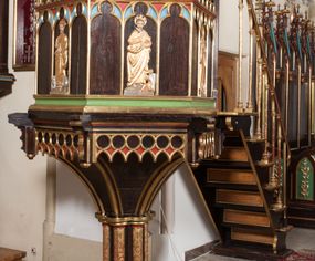 Zdjęcie nr 1: Ambona wolnostojąca, dostępna schodkami od strony prezbiterium, z pulpitem do czytania. Kosz sześcioboczny ustawiony na postumencie o przekroju wieloliścia utworzonym z wiązki kolumienek o złoconych bazach i trzonach zdobionych rytym ornamentem roślinnym, osadzonym na niskim, sześciobocznym cokole. U podstawy kosza ostrołukowy fryz arkadkowy. Ścianki kosza podzielone na trzy części dekoracją pseudomaswerkową w formie arkadek. W środkowej arkadce każdego z pól płaskorzeźbione, polichromowane i złocone przedstawienie ewangelistów:  św. Jana, św. Mateusza, św. Marka i św. Łukasza. Powyżej fryz ze stylizowanych lilii heraldycznych. Schody jednobiegowe, z balustradą utworzoną z rzędu wąskich kolumienek, ustawionych na niskich cokołach i bazach, o złoconych trzonach i półkolistych kapitelach. Każdy z ewangelistów ukazany całopostaciowo, frontalnie, z księgą w lewej ręce i piórem w prawej. U stóp ewangelistów przedstawiono odpowiadające im atrybuty: św. Marka – lew, św. Jana – orzeł, św. Mateusza – człowiek, św. Łukasza - wół. Ewangeliści, oprócz św. Jana mają rysy twarzy dojrzałych mężczyzn, z brodami, św. Jan bez brody z długimi i jasnymi włosami, opadającymi na plecy. Ubrani są w długie złocone suknie i złocone płaszcze. Struktura malowana na ciemny brąz, płyciny na kolor niebieski, zielony i czerwony, partie ornamentu złocone. 