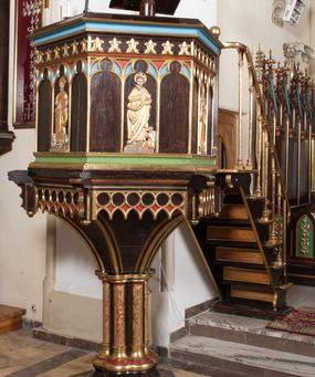 Zdjęcie nr 1: Ambona wolnostojąca, dostępna schodkami od strony prezbiterium, z pulpitem do czytania. Kosz sześcioboczny ustawiony na postumencie o przekroju wieloliścia utworzonym z wiązki kolumienek o złoconych bazach i trzonach zdobionych rytym ornamentem roślinnym, osadzonym na niskim, sześciobocznym cokole. U podstawy kosza ostrołukowy fryz arkadkowy. Ścianki kosza podzielone na trzy części dekoracją pseudomaswerkową w formie arkadek. W środkowej arkadce każdego z pól płaskorzeźbione, polichromowane i złocone przedstawienie ewangelistów:  św. Jana, św. Mateusza, św. Marka i św. Łukasza. Powyżej fryz ze stylizowanych lilii heraldycznych. Schody jednobiegowe, z balustradą utworzoną z rzędu wąskich kolumienek, ustawionych na niskich cokołach i bazach, o złoconych trzonach i półkolistych kapitelach. Każdy z ewangelistów ukazany całopostaciowo, frontalnie, z księgą w lewej ręce i piórem w prawej. U stóp ewangelistów przedstawiono odpowiadające im atrybuty: św. Marka – lew, św. Jana – orzeł, św. Mateusza – człowiek, św. Łukasza - wół. Ewangeliści, oprócz św. Jana mają rysy twarzy dojrzałych mężczyzn, z brodami, św. Jan bez brody z długimi i jasnymi włosami, opadającymi na plecy. Ubrani są w długie złocone suknie i złocone płaszcze. Struktura malowana na ciemny brąz, płyciny na kolor niebieski, zielony i czerwony, partie ornamentu złocone. 