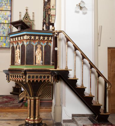 Zdjęcie nr 2: Ambona wolnostojąca, dostępna schodkami od strony prezbiterium, z pulpitem do czytania. Kosz sześcioboczny ustawiony na postumencie o przekroju wieloliścia utworzonym z wiązki kolumienek o złoconych bazach i trzonach zdobionych rytym ornamentem roślinnym, osadzonym na niskim, sześciobocznym cokole. U podstawy kosza ostrołukowy fryz arkadkowy. Ścianki kosza podzielone na trzy części dekoracją pseudomaswerkową w formie arkadek. W środkowej arkadce każdego z pól płaskorzeźbione, polichromowane i złocone przedstawienie ewangelistów:  św. Jana, św. Mateusza, św. Marka i św. Łukasza. Powyżej fryz ze stylizowanych lilii heraldycznych. Schody jednobiegowe, z balustradą utworzoną z rzędu wąskich kolumienek, ustawionych na niskich cokołach i bazach, o złoconych trzonach i półkolistych kapitelach. Każdy z ewangelistów ukazany całopostaciowo, frontalnie, z księgą w lewej ręce i piórem w prawej. U stóp ewangelistów przedstawiono odpowiadające im atrybuty: św. Marka – lew, św. Jana – orzeł, św. Mateusza – człowiek, św. Łukasza - wół. Ewangeliści, oprócz św. Jana mają rysy twarzy dojrzałych mężczyzn, z brodami, św. Jan bez brody z długimi i jasnymi włosami, opadającymi na plecy. Ubrani są w długie złocone suknie i złocone płaszcze. Struktura malowana na ciemny brąz, płyciny na kolor niebieski, zielony i czerwony, partie ornamentu złocone. 