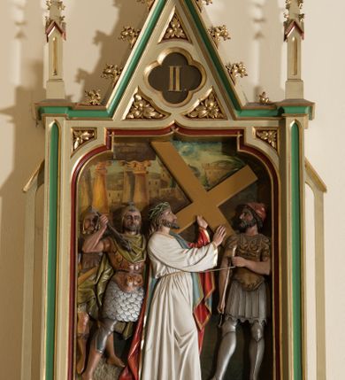 Zdjęcie nr 2: Czternaście płaskorzeźbionych, polichromowanych stacji drogi krzyżowej ukazanych na tle malowanego pejzażu. Przedstawienia ujęte w neogotyckie, architektoniczne ramy zamknięte wimpergą z żabkami, zwieńczoną  kwiatonem z krzyżem, pośrodku wimpergi czterolistna płycina z numerem stacji. Wnęka na płaskorzeźbę zamknięta łukiem dwuramiennym. Partia cokołowa ujęta od dołu podwieszeniem z rozetką. Polichromia ram w odcieniu kremowym, zielonym i ciemnoczerwonym z pozłacanym detalem. Sceny wielofigurowe z Chrystusem w centrum. Chrystus na większości przedstawień jest ubrany w długą, białą tunikę z pozłacaną lamówką i czerwony płaszcz z błękitną podszewką. Twarz owalna okolona ciemnymi włosami i ciemnym zarostem. W tle pejzaż z elementami architektury. Na stacji pierwszej, w prawym dolnym rogu napis „Ferd(inand) Stuflesser / Bildabauer / S(ank)t Ulrich Gröden Tirol / 1903”.