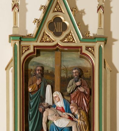 Zdjęcie nr 6: Czternaście płaskorzeźbionych, polichromowanych stacji drogi krzyżowej ukazanych na tle malowanego pejzażu. Przedstawienia ujęte w neogotyckie, architektoniczne ramy zamknięte wimpergą z żabkami, zwieńczoną  kwiatonem z krzyżem, pośrodku wimpergi czterolistna płycina z numerem stacji. Wnęka na płaskorzeźbę zamknięta łukiem dwuramiennym. Partia cokołowa ujęta od dołu podwieszeniem z rozetką. Polichromia ram w odcieniu kremowym, zielonym i ciemnoczerwonym z pozłacanym detalem. Sceny wielofigurowe z Chrystusem w centrum. Chrystus na większości przedstawień jest ubrany w długą, białą tunikę z pozłacaną lamówką i czerwony płaszcz z błękitną podszewką. Twarz owalna okolona ciemnymi włosami i ciemnym zarostem. W tle pejzaż z elementami architektury. Na stacji pierwszej, w prawym dolnym rogu napis „Ferd(inand) Stuflesser / Bildabauer / S(ank)t Ulrich Gröden Tirol / 1903”.